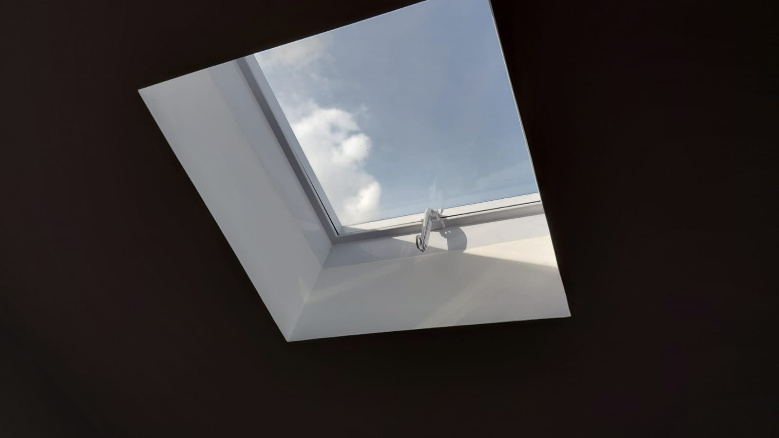 Skylight in a dark ceiling — crisp white upstand framing a perfect blue sky view