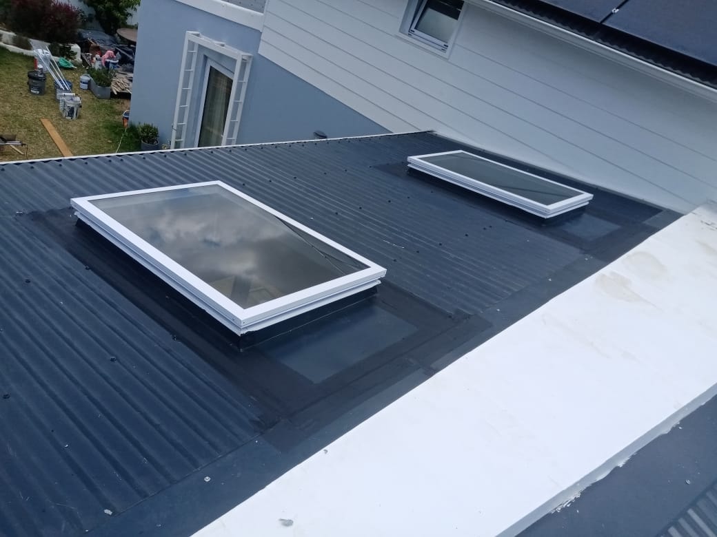 Two white-framed skylights installed on a dark corrugated IBR roof