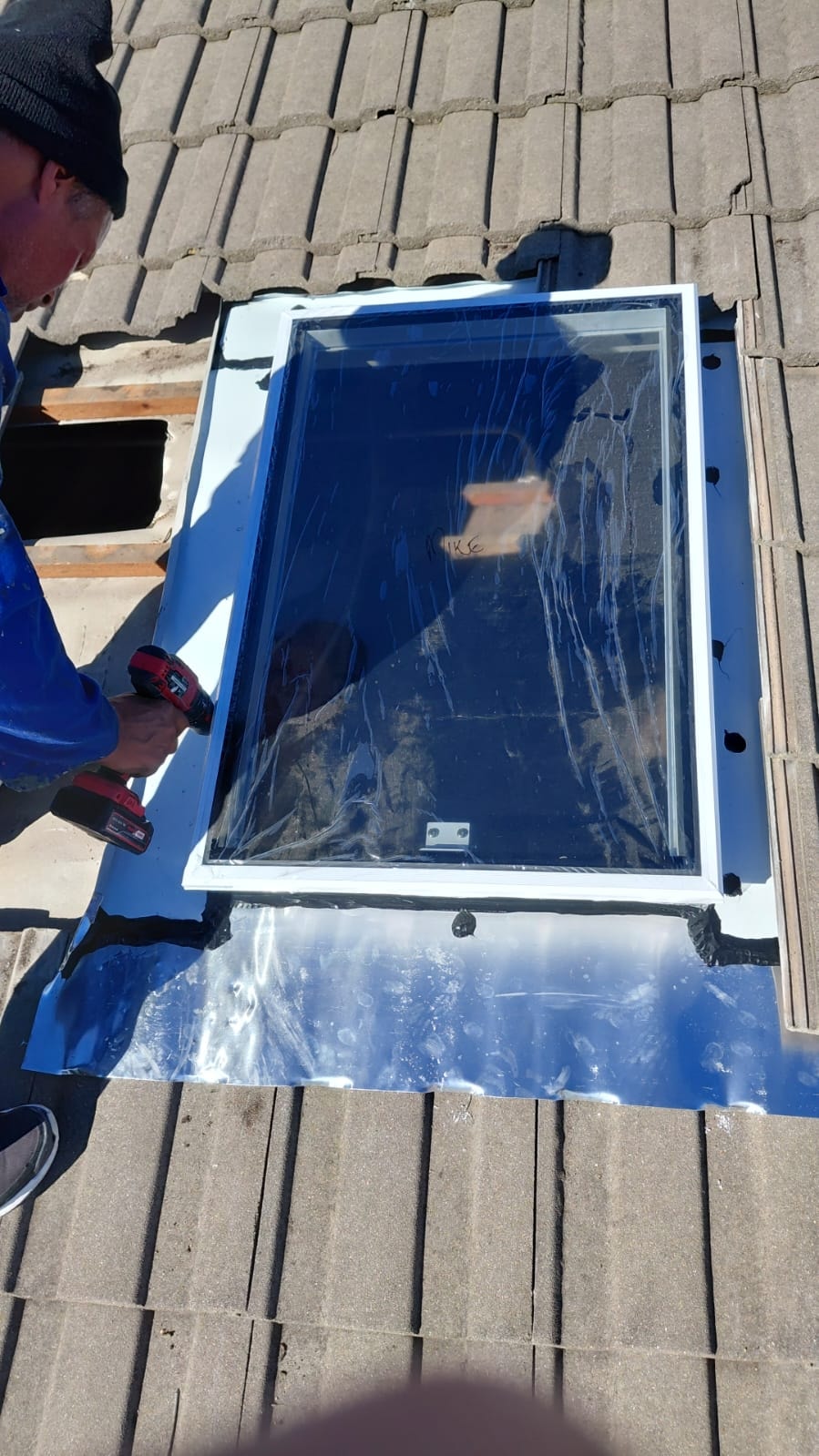 RWI technician fitting a skylight unit on a tiled roof — precision workmanship on site